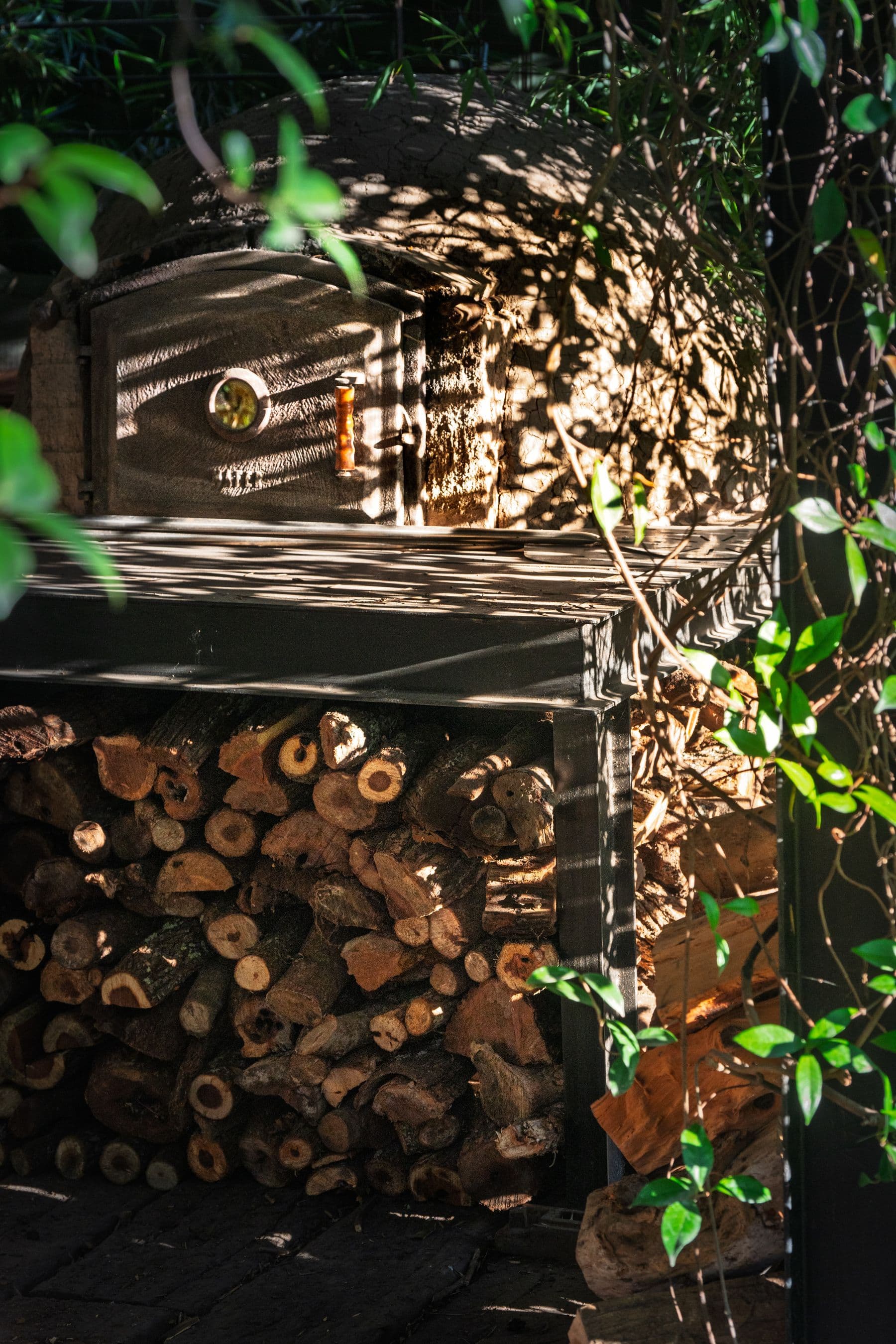 An outdoor wood-fired oven with stacked firewood