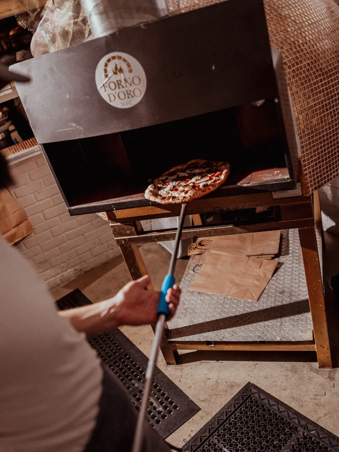 A pizza going into the wood-fired oven on a peel